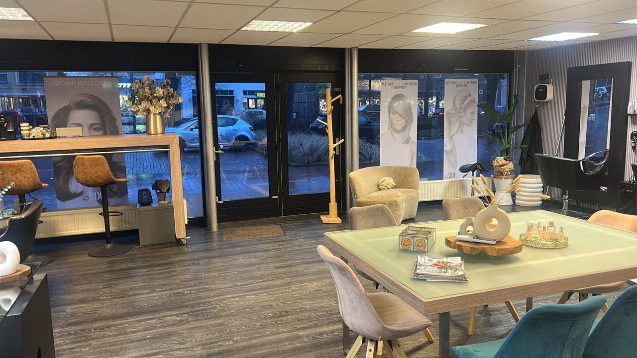 De salon van binnen, met de glazen pui, een zithoek en de tafel